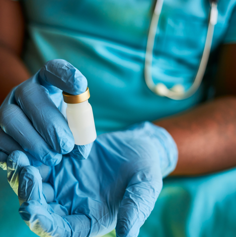 A healthcare professional holds a vaccine vial in their hands. They are wearing blue medical gloves
