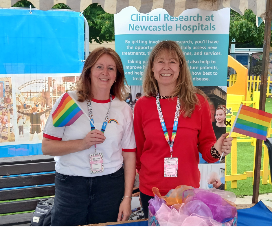 Two people stand holding a rainbow flag 
