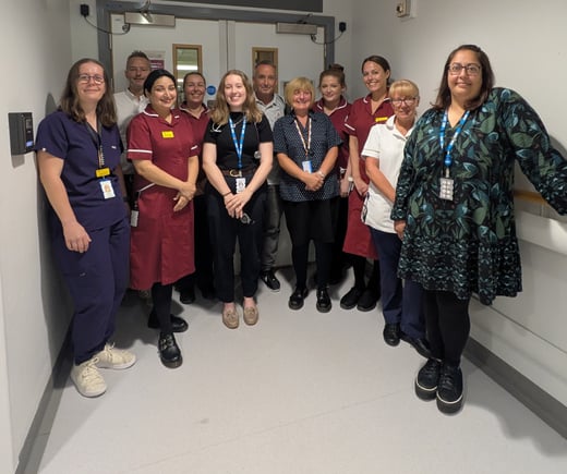 A team of clinical and support staff stand in a hospital corridor with Graeme 